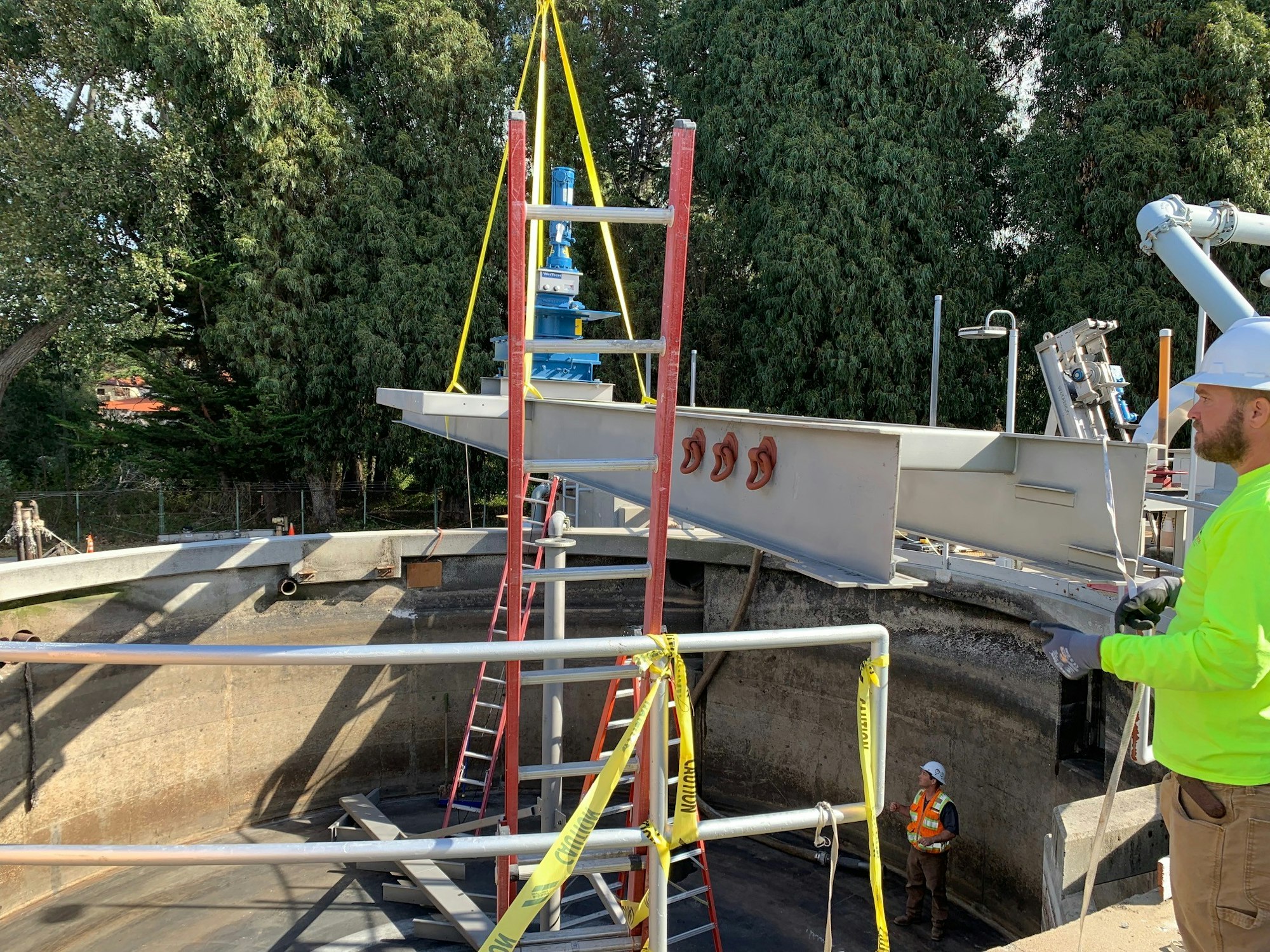 The image shows construction work at a site with a crane, metal structures, and workers in safety gear.