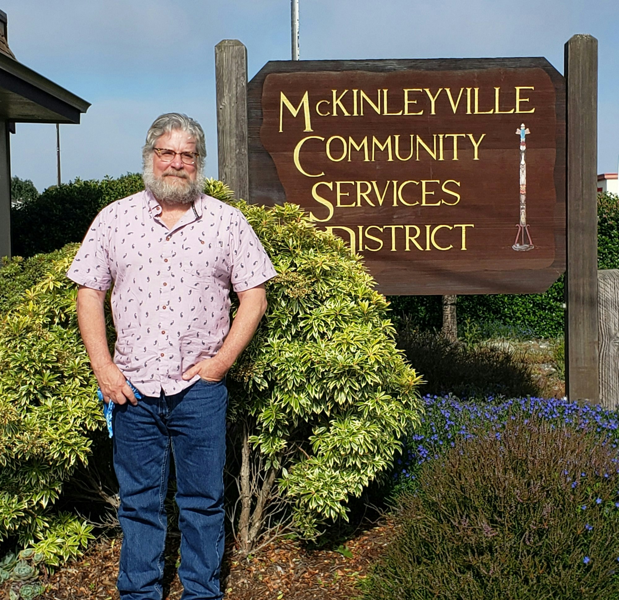 A man stands in front of the McKinleyville Community Services District sign, surrounded by bushes.