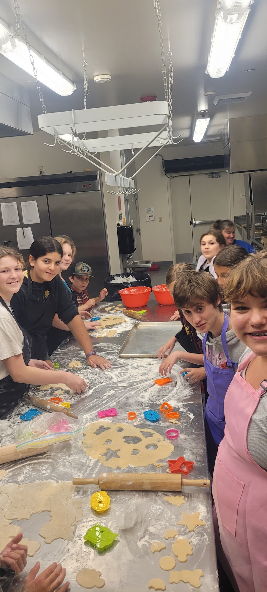 A group of kids in a kitchen making cookies with dough and colorful cutters.