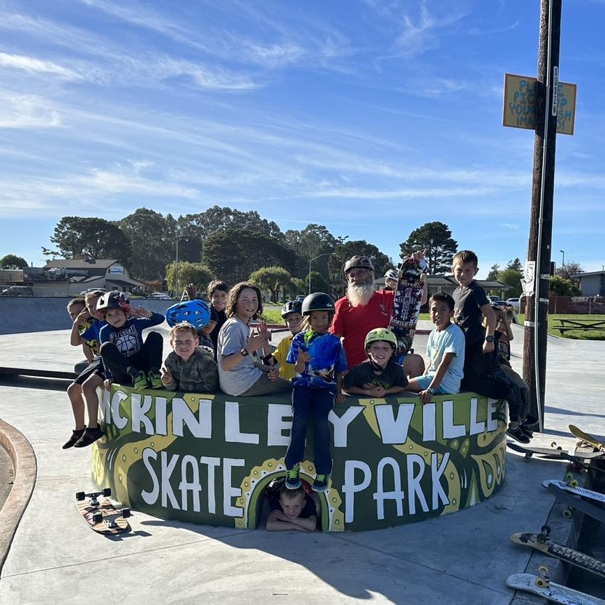 Group of people, mostly children, at a skate park with skateboards, posing for a photo.