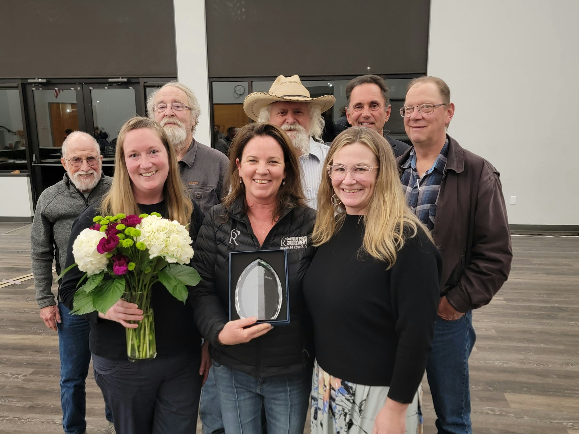 A group of people poses for a photo, celebrating a woman receiving an award and holding flowers.