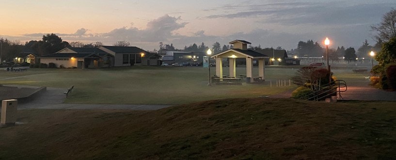 A quiet park at dawn, with a gazebo, grassy area, benches, and soft lighting. Fog adds a serene atmosphere.