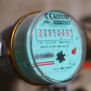 The image shows a water meter with a digital display, measuring water usage, and includes identification numbers.