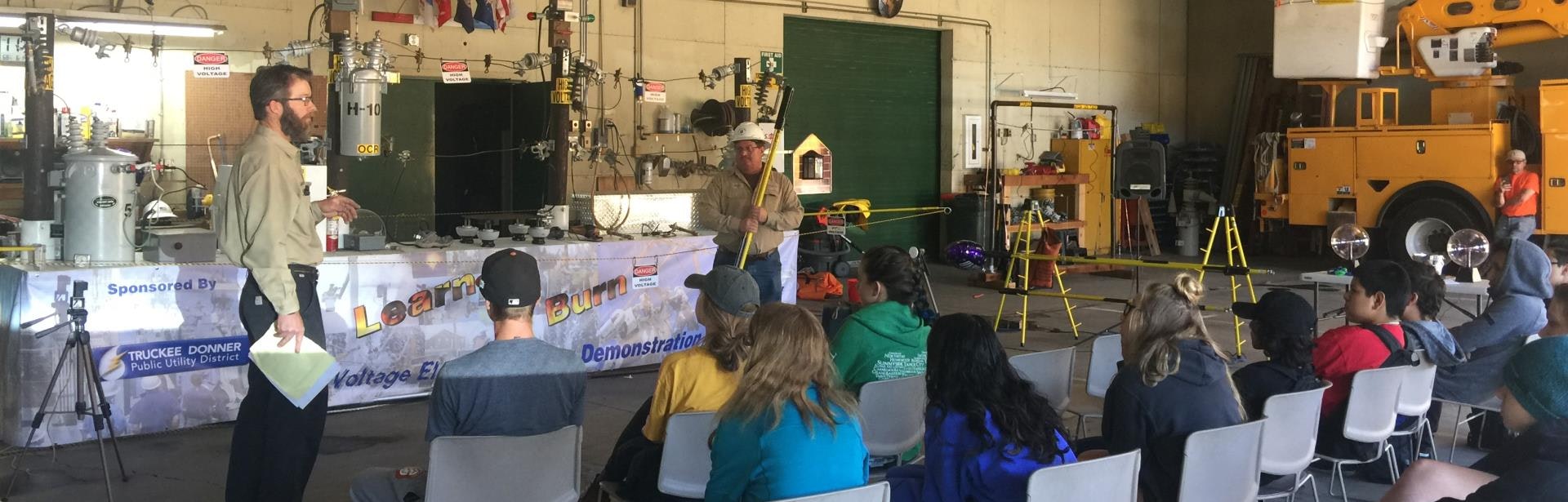 A demonstration on electrical safety for an audience, featuring equipment and instructors in a utility setting.
