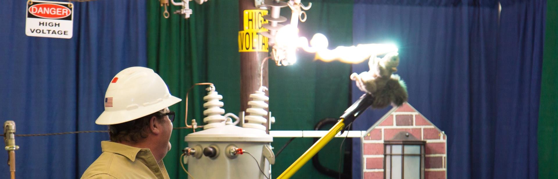A worker in a hard hat observes a high-voltage demonstration with electrical arcs, showcasing safety and risk.