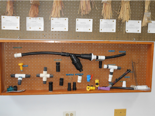 The image shows a pegboard with various plumbing fittings, connectors, and tools organized for display.
