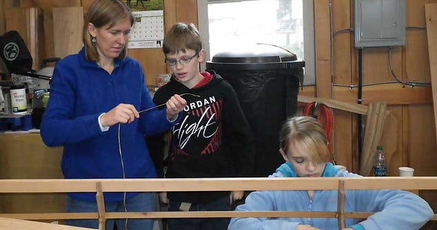 Adult and children with a yarn and frame, likely doing a craft or educational activity.