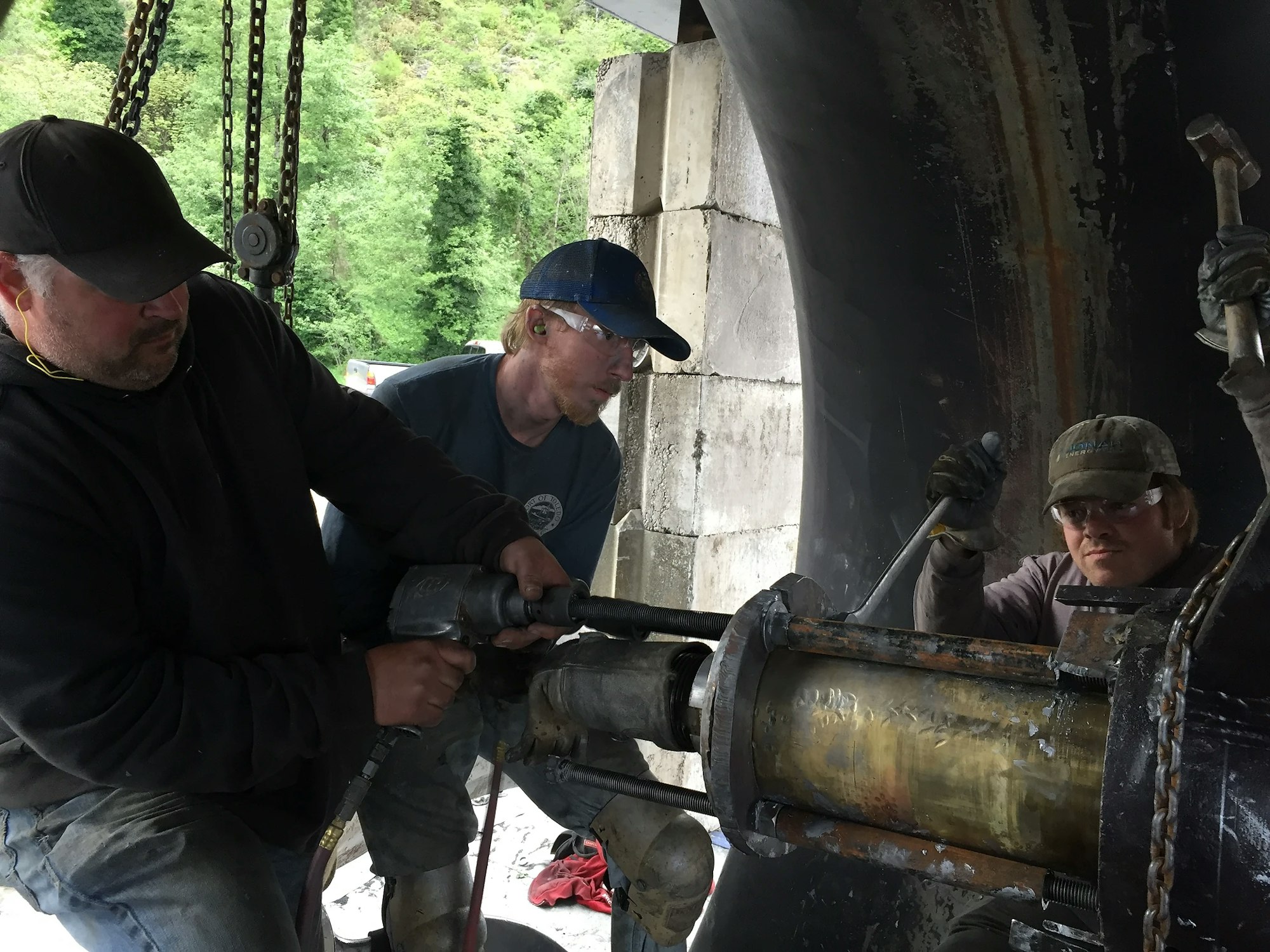 Three workers using tools on machinery, likely maintenance or repair work.