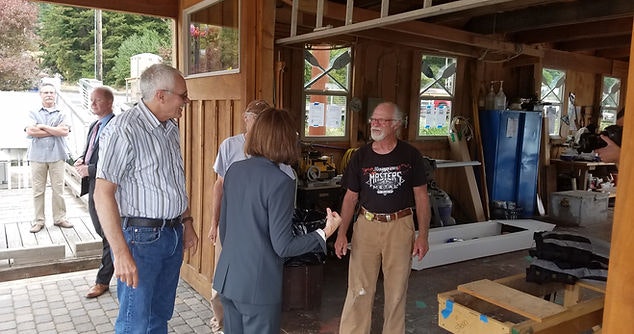 People in a workshop with tools and equipment, some shaking hands, possibly a professional or social meeting.