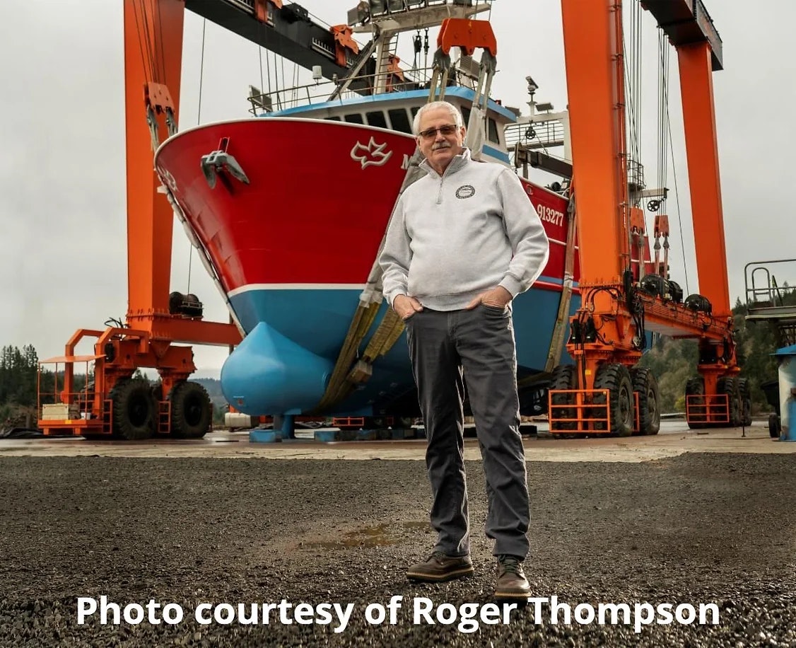 Man stands in front of a large ship being held by an orange mobile boat hoist.