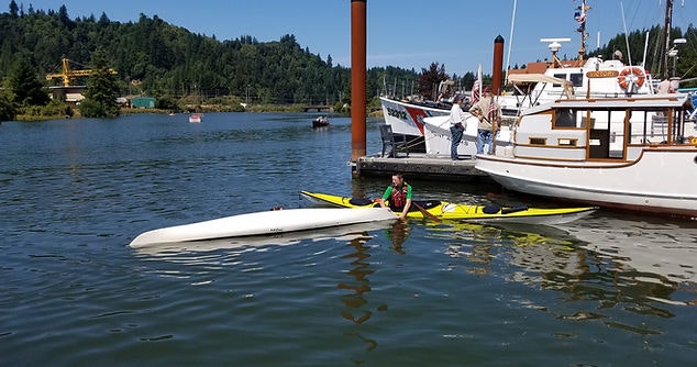 A person kayaking near a dock with boats under a clear blue sky.
