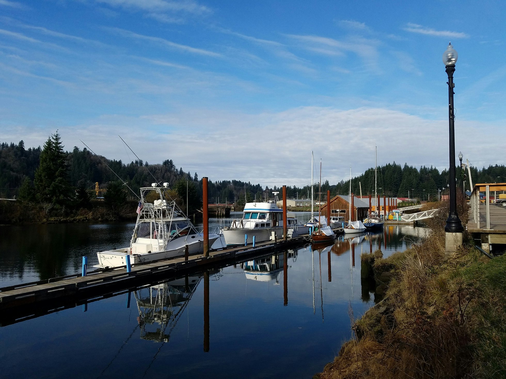 A tranquil marina with boats docked, a clear sky, and reflections on calm water.