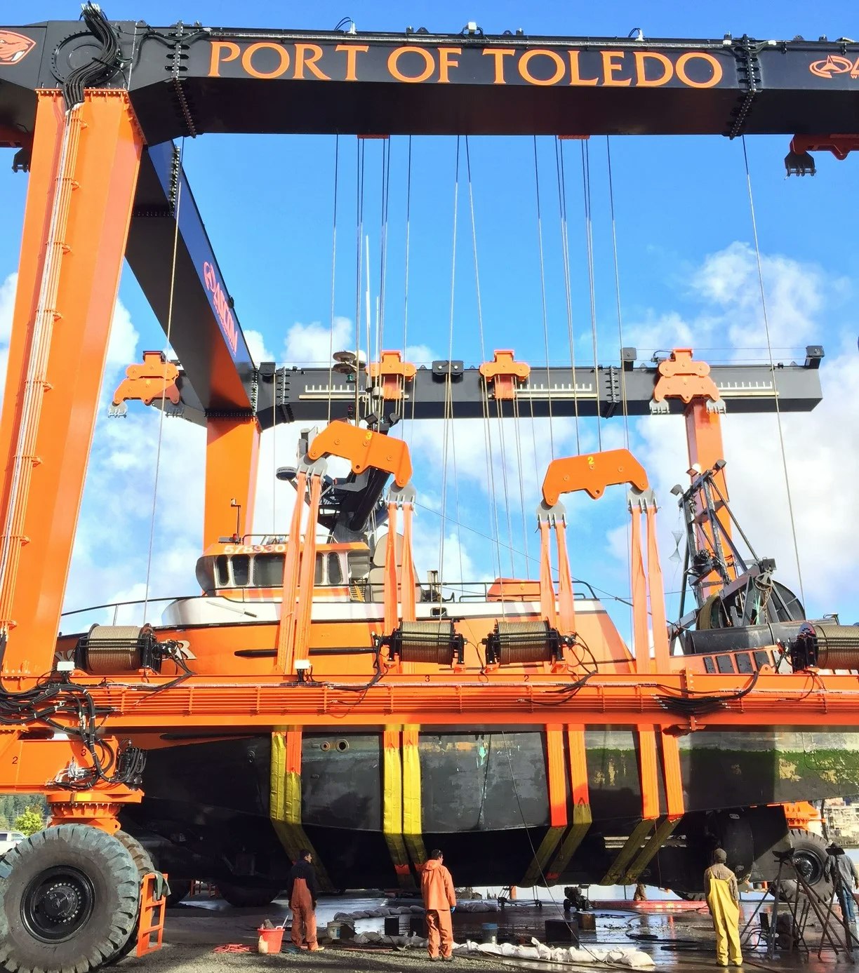 A large orange ship lift at Port of Toledo with workers below.