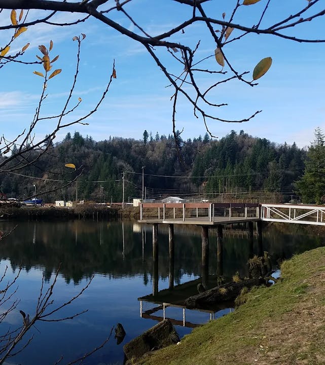 A serene river scene with a pier, trees, and clear sky.