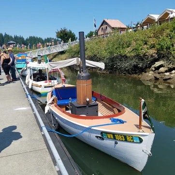 A steamboat model moored at a dock with people and buildings in the background.