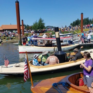 Wooden boats on water with people, spectators onshore, clear sky.