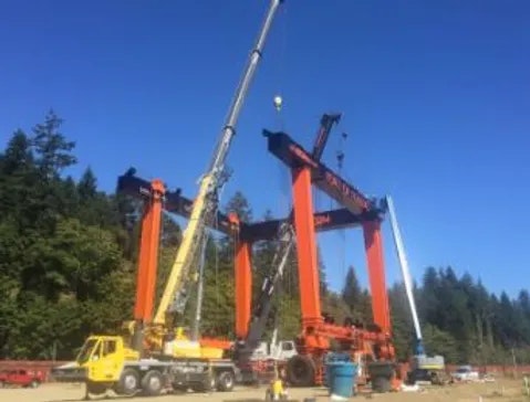 Two large cranes operating beside a structure under a clear sky.