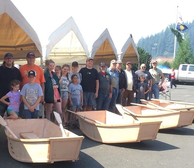 Group of people posing with handmade wooden boats under tents, outdoors on a sunny day.
