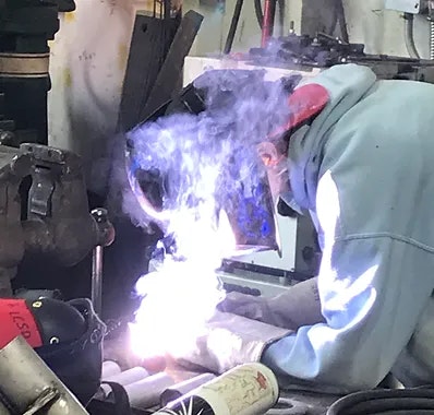 A person welding with gear on, bright light and smoke visible.