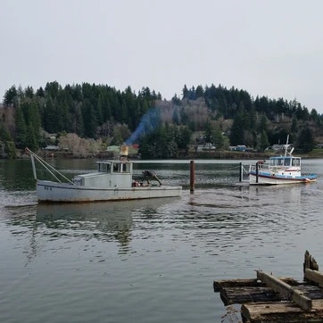 Two boats on a calm river with trees in the background and a jetty in the foreground.