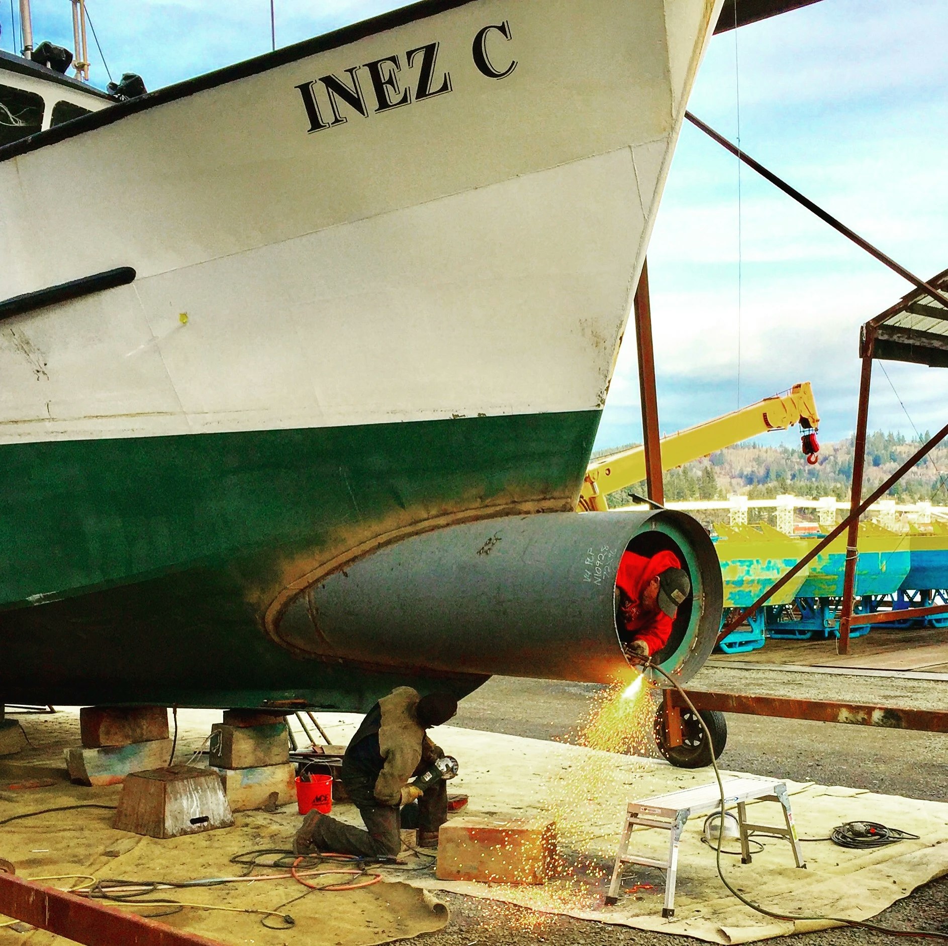 A worker is welding near the propeller of a large boat, "INEZ C," on land possibly for repairs or maintenance.