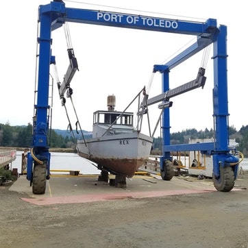 A boat named "REX" lifted by a large blue boat hoist at Port of Toledo.