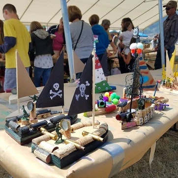 Handmade model boats on a table at a craft fair, with people in the background.