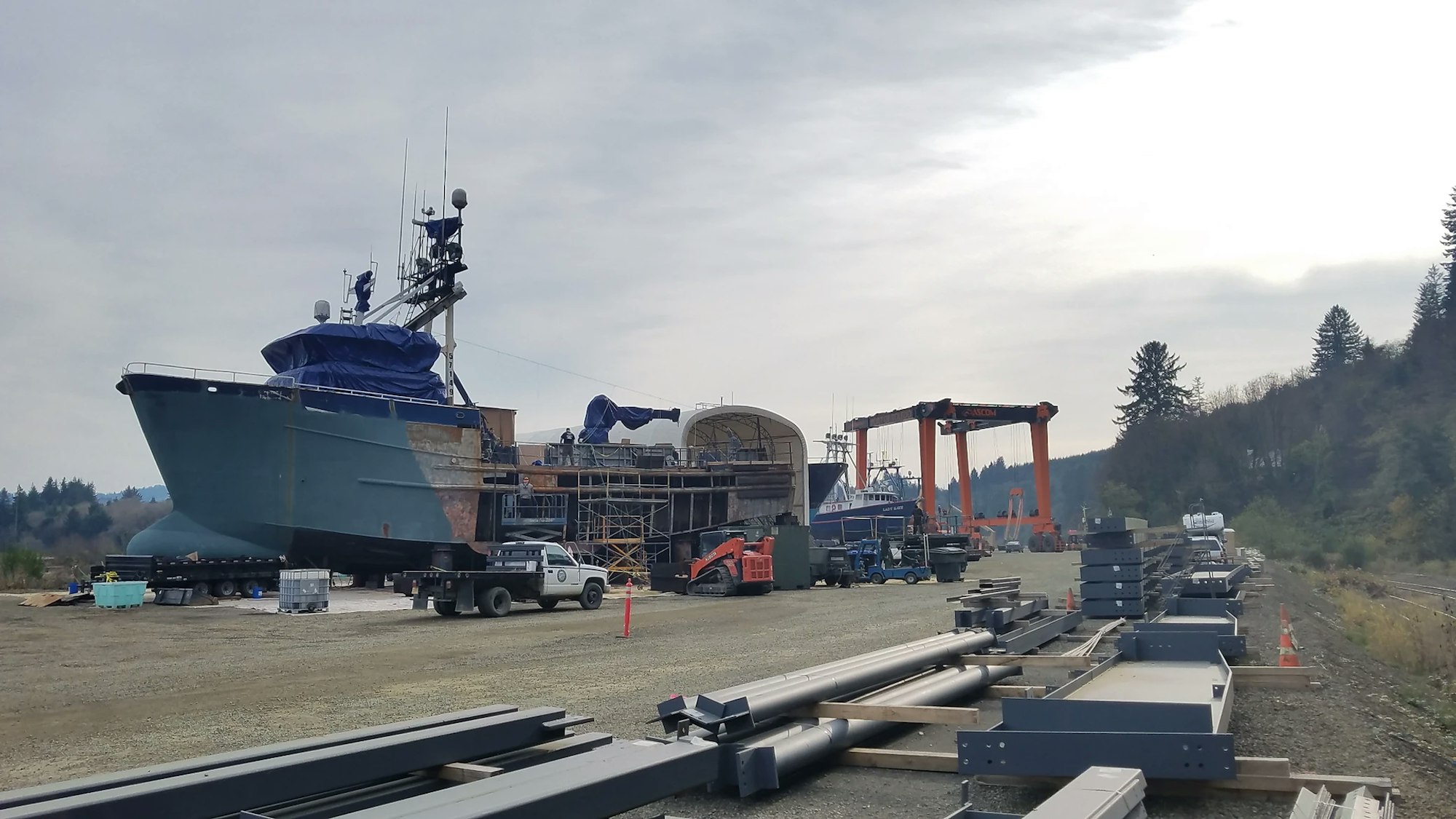 A shipyard with boats being repaired or built, surrounded by construction materials and equipment.