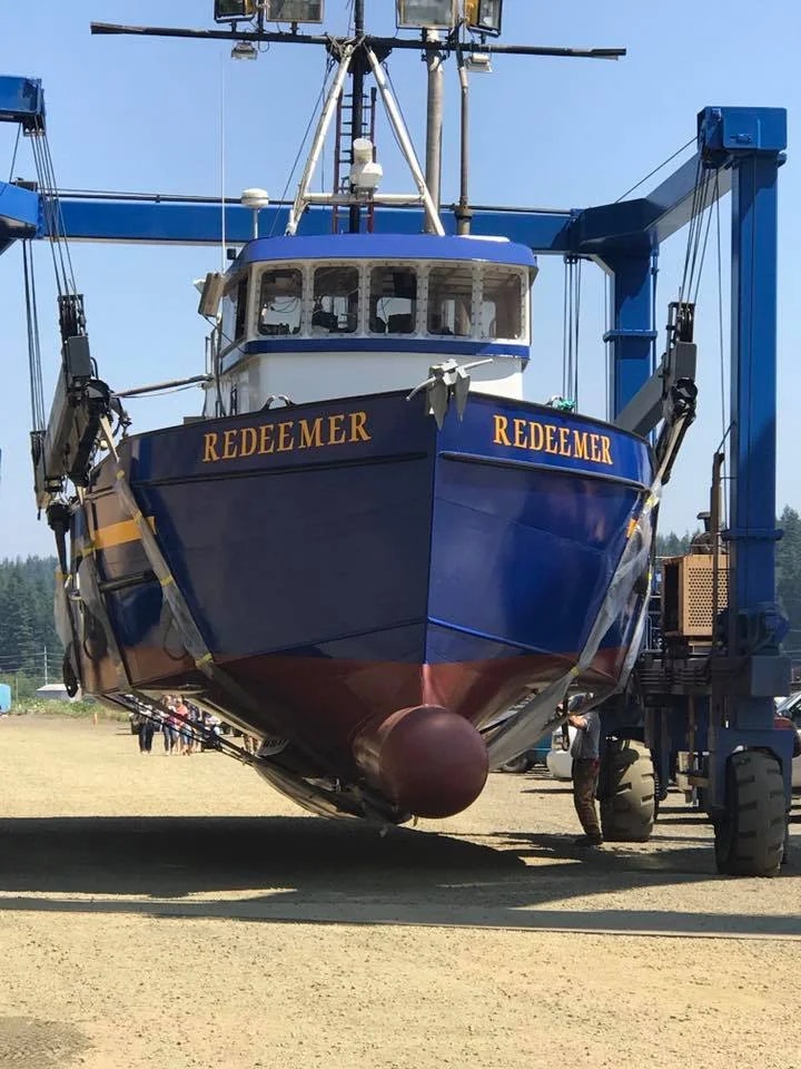 A boat named REDEEMER being lifted by a blue crane mechanism.