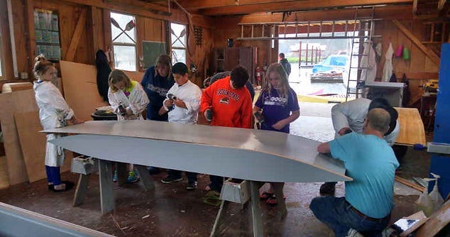 Group of people around a large metal piece, working together in a workshop environment.