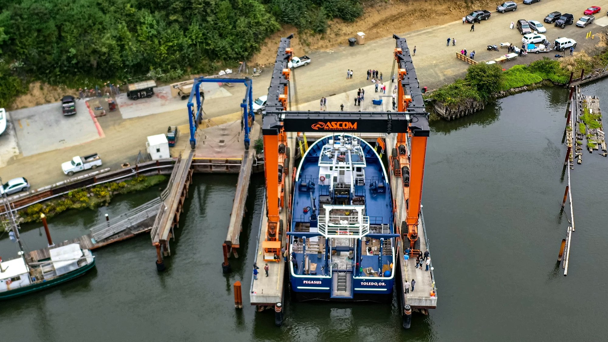 Aerial view of an industrial vessel docked at a pier with nearby vehicles and people.