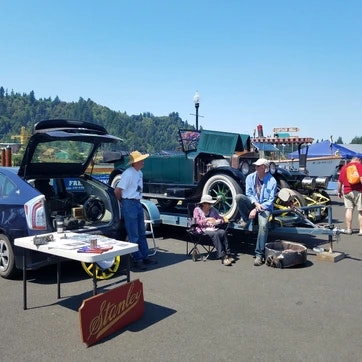 Outdoor car exhibition with people, classic car, displays, under a clear sky.