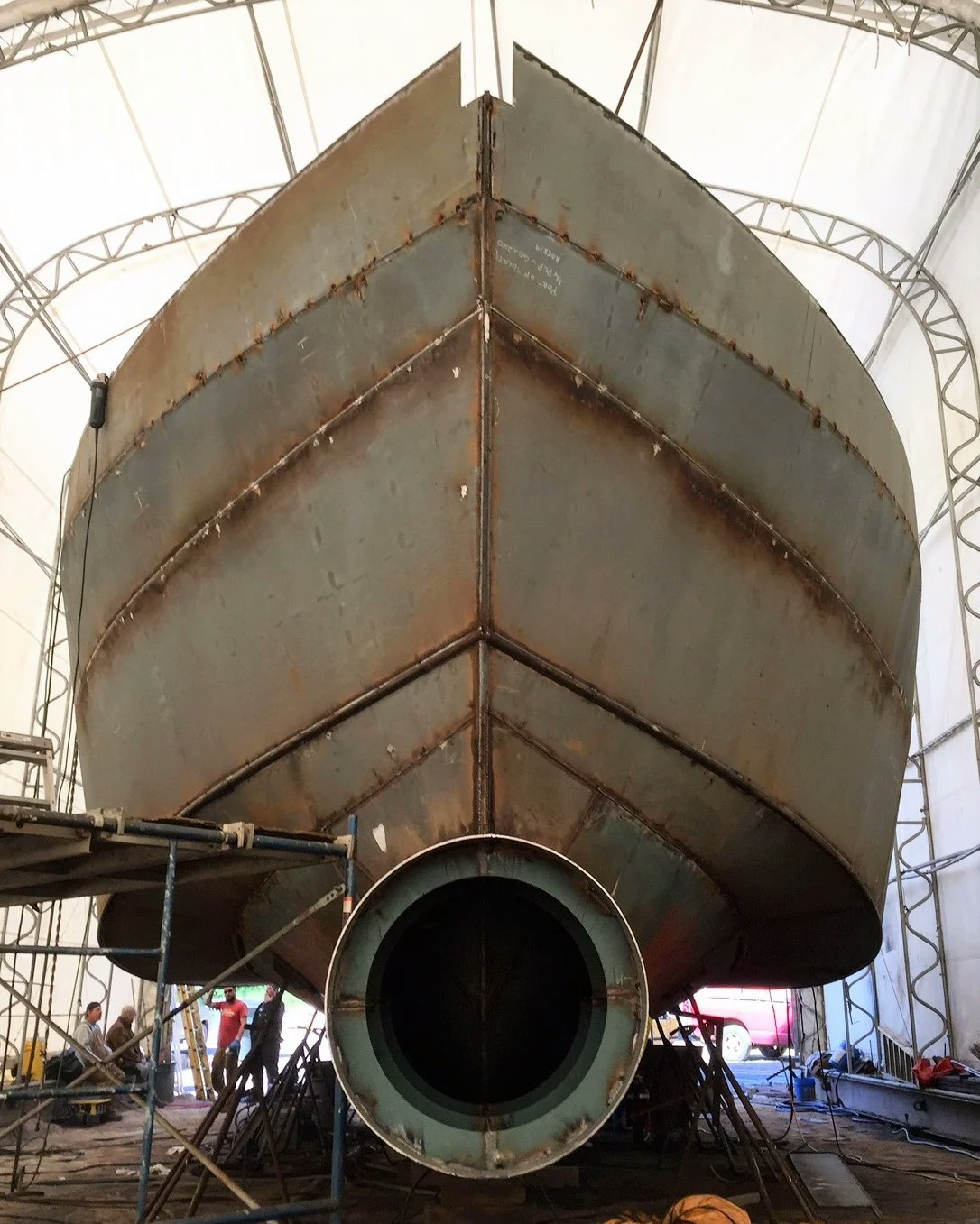 A large ship under construction or repair in a dry dock with scaffolding.