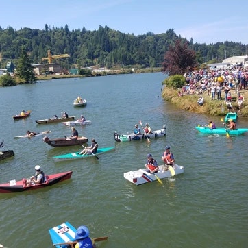 A river event with people in various boats, a watching crowd on the shore, and a sunny day.