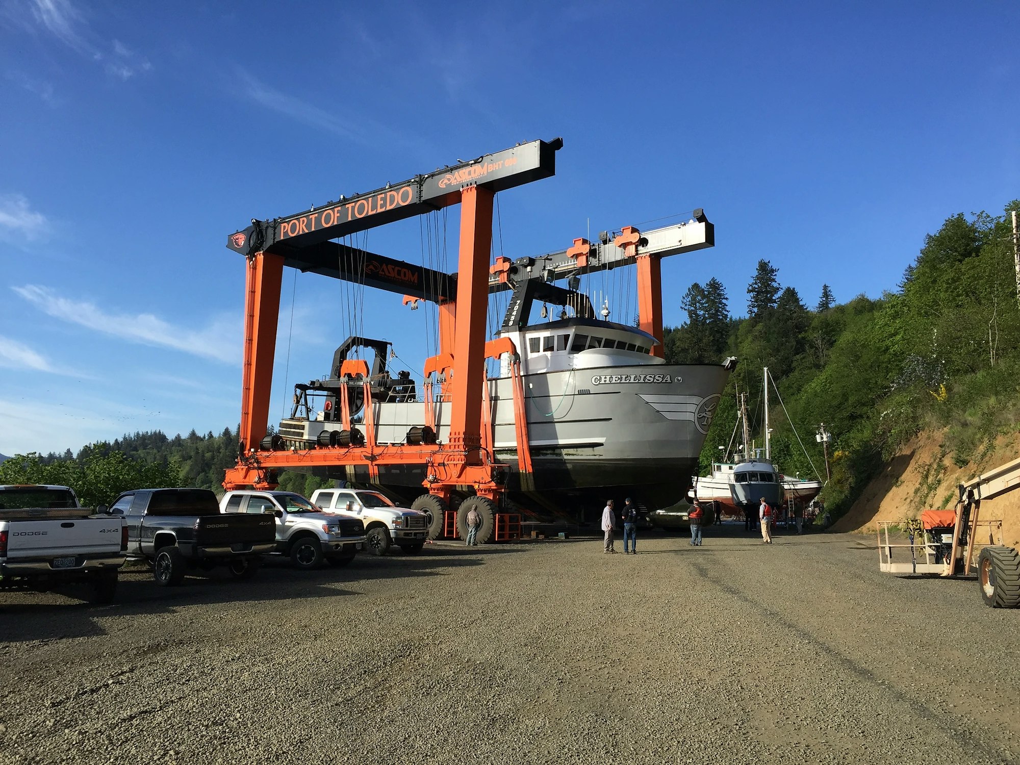 A large orange boat lift at Port of Toledo holding a boat named "Chelsea K", with people and vehicles around on a sunny day.