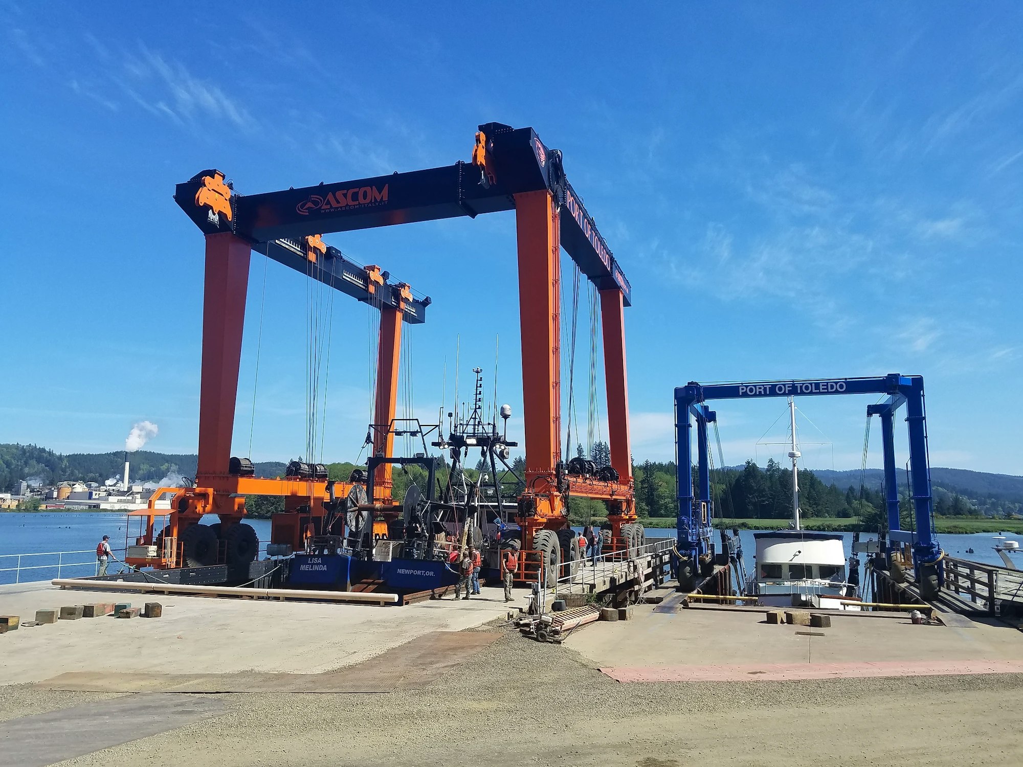 A large orange gantry crane at a port with "PORT OF TOLEDO" sign, clear blue sky, and boats.