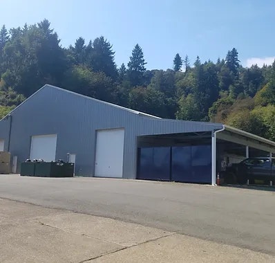 A large warehouse with open and closed bays and surrounding trees under a clear sky.