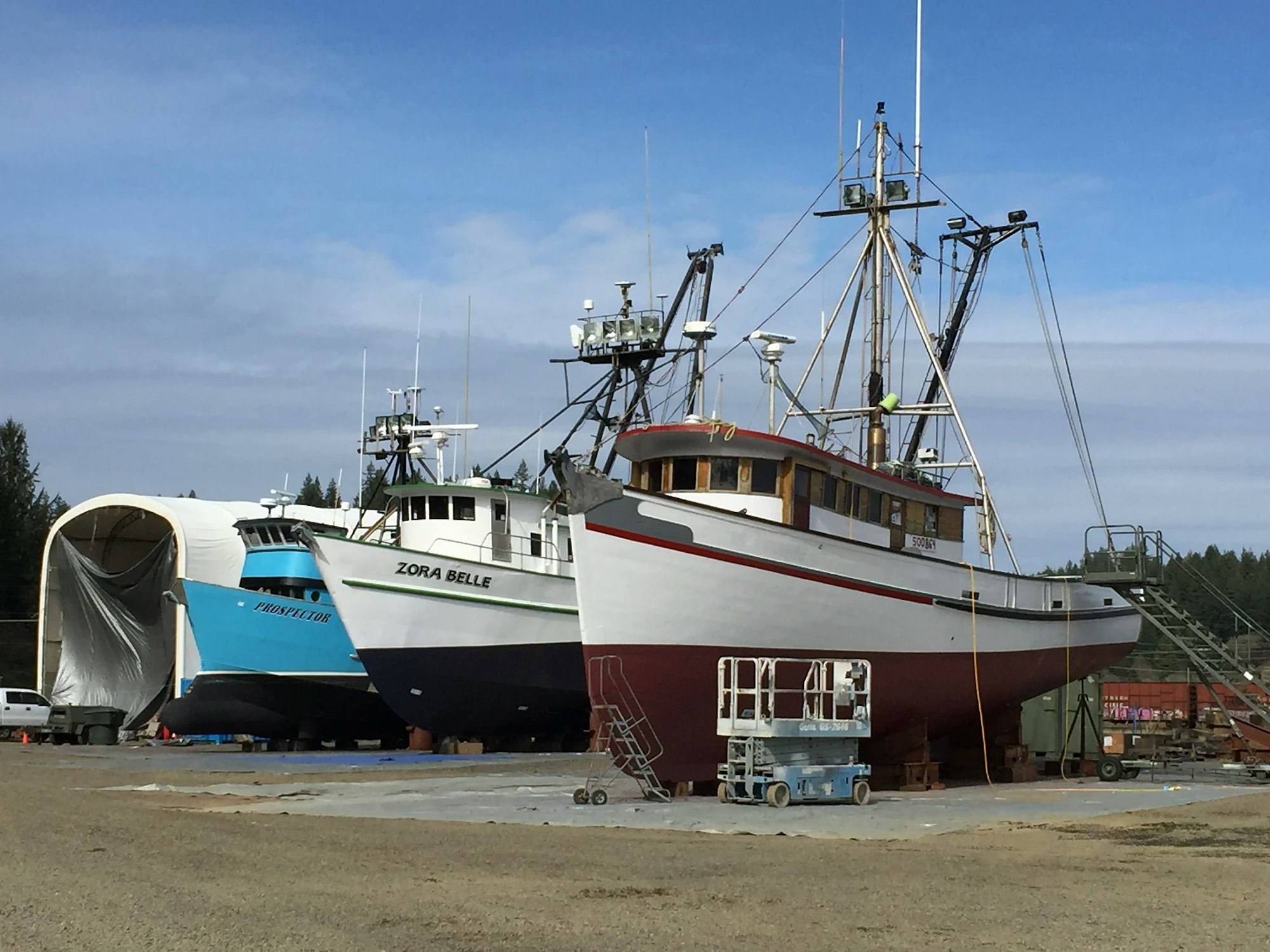 Fishing boats in dry dock for maintenance or repair, clear skies, and forestry in the background.