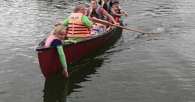 People in a canoe, one leaning over the side, likely reaching for something in the water.