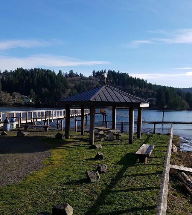 A gazebo by a lake with a dock, surrounded by trees under a clear sky.