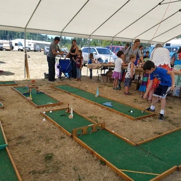 A miniature golf setup under a tent with people playing and observing.