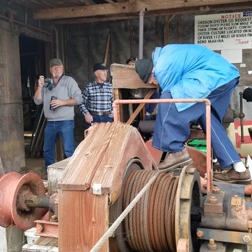 Three people by old machinery, likely in a rustic workshop or garage.