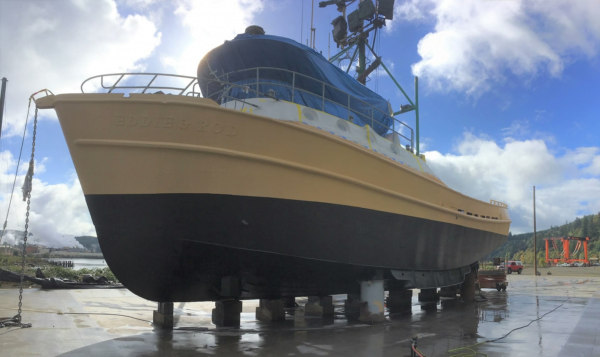 A large boat named EUDIE & ROD on dry dock, partly covered, with a sunny, cloudy sky in the background.