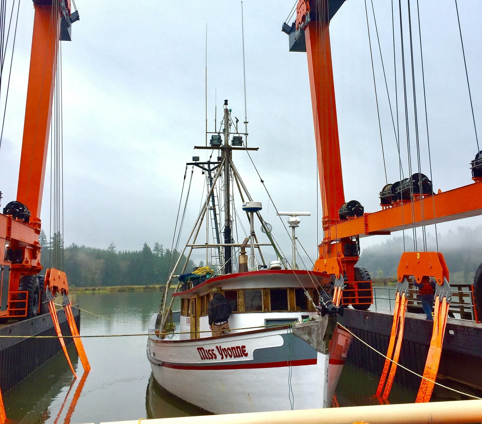 Fishing boat being lifted by an orange marine travelift on a cloudy day.