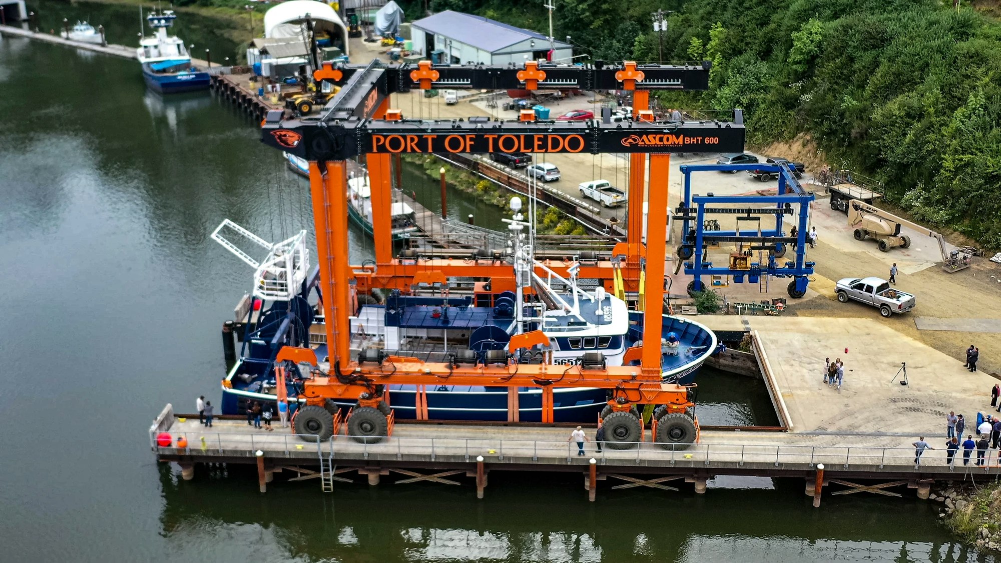 Aerial view of Port of Toledo with a boat lift handling a vessel, people around, and structures nearby.