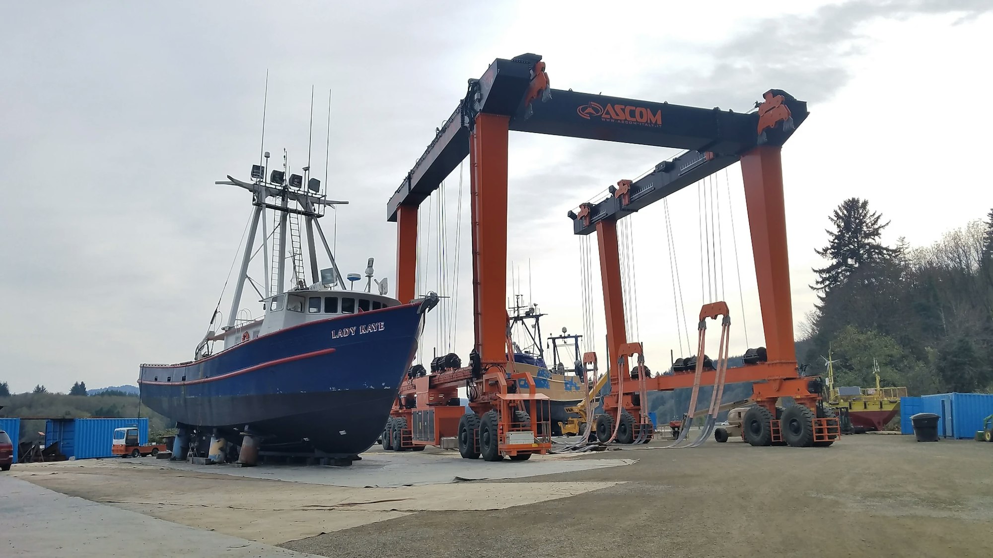 A fishing boat named "LADY KAYE" lifted by a large orange mobile boat hoist at a shipyard.