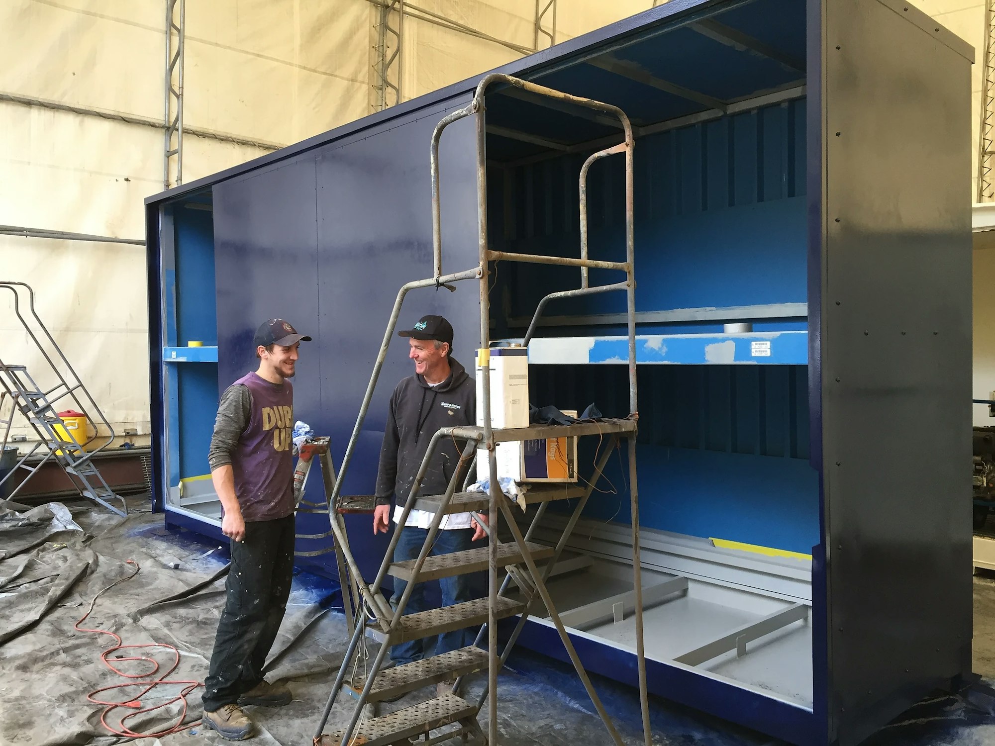 Two people next to a large blue industrial shelf, with painting equipment and smiles.
