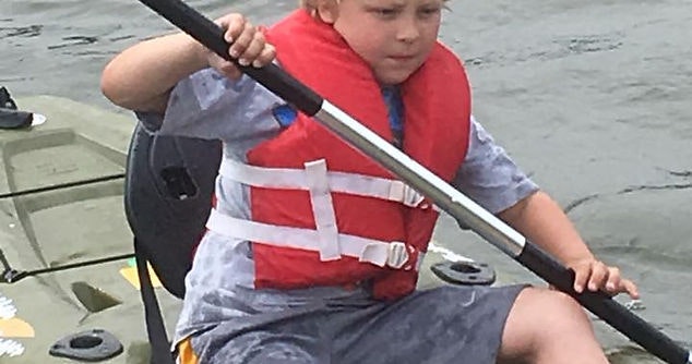 A child in a life vest paddling a kayak.