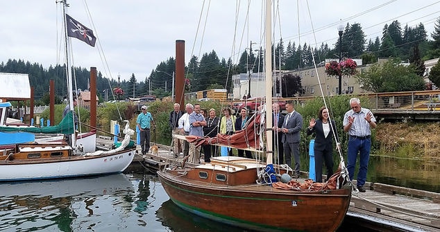 A group of people on a dock next to a vintage wooden boat with sails down.