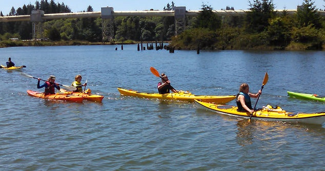 People kayaking on a river with a bridge in the background.